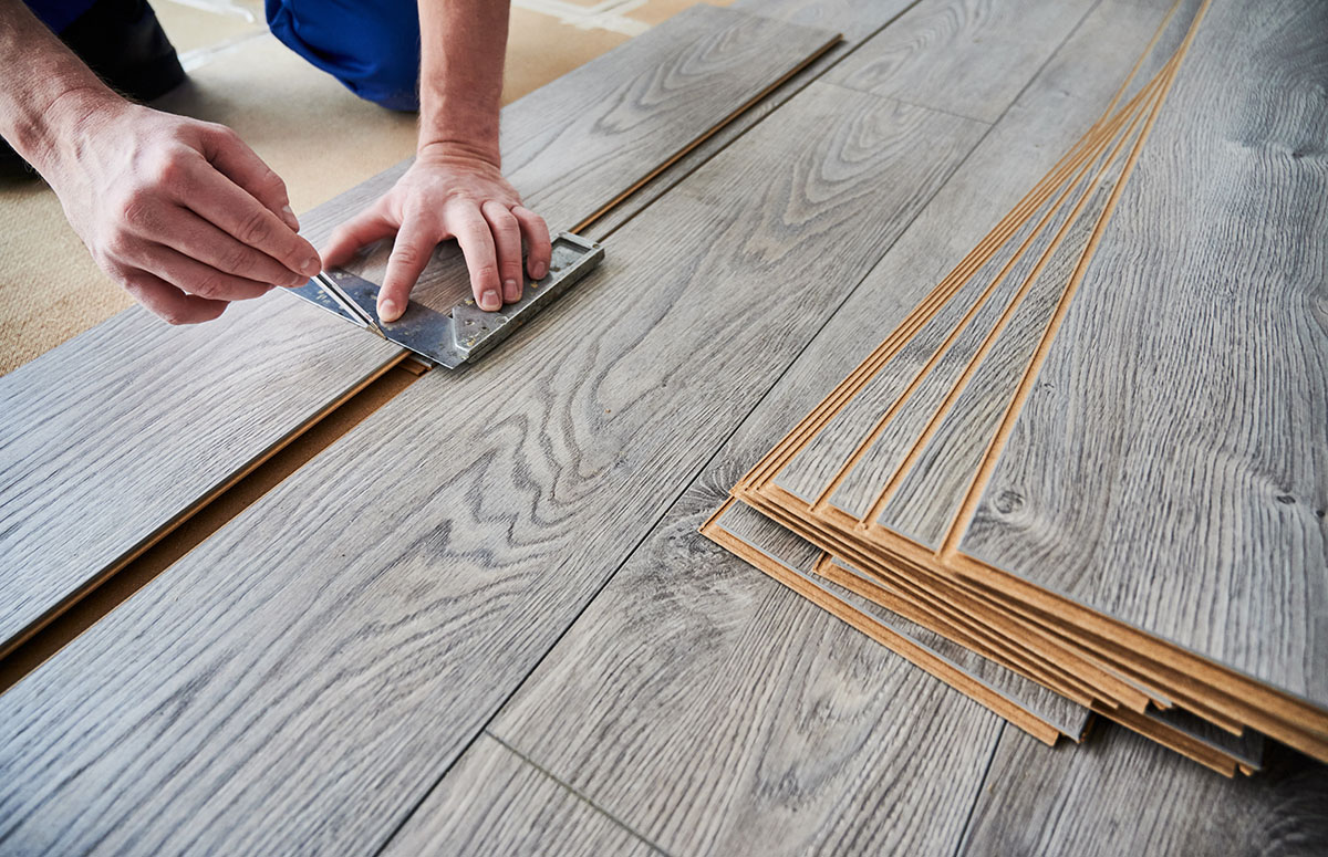 Male worker hands drawing line on laminate wood plank.